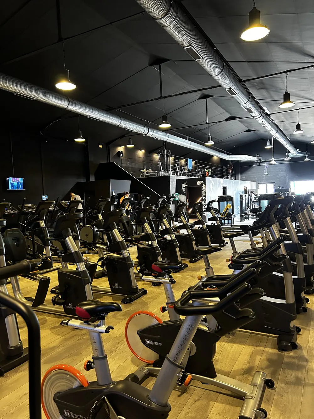 Plateau cardio rempli de vélos sous mezzanine et écrans
